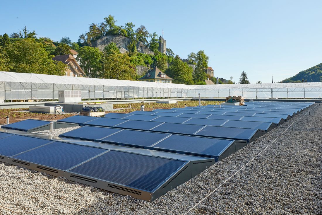 Flachdach mit flachen Photovoltaik-Modulen auf Kiesdeckung in Aargau, umgeben von Natur und historischen Gebäuden